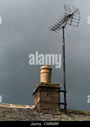 Landhaus Stein Kamin und Teil der Schieferdach mit TV Antenne vor einem dunklen grüblerischen Himmel Stockfoto