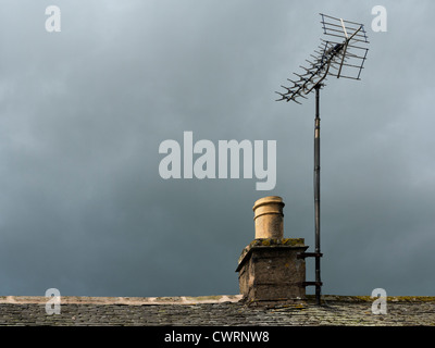 Landhaus Stein Kamin und Teil der Schieferdach mit TV Antenne vor einem dunklen grüblerischen Himmel Stockfoto
