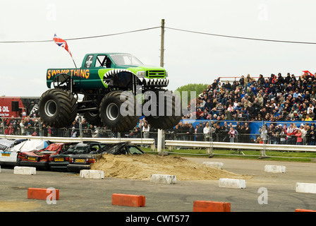 Ein Monstertruck namens "Swamp Thing" bei einer Show auf dem Santa Pod Raceway über eine Reihe von Autos zu springen. Stockfoto