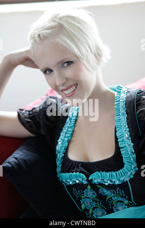 Lächelnde junge Frau auf Couch ein Dirndl tragen Stockfoto