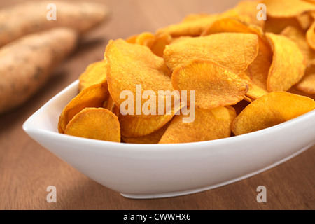 Knusprige peruanischen Süßkartoffel-chips in weiße Keramikschale mit Süßkartoffeln in den Rücken Stockfoto