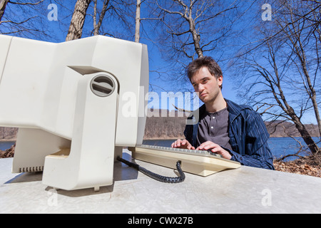 Ein junger Mann Tippen auf seinem Computer in der Natur und umgeben von Bäumen, Mutter Natur und einen wunderschönen blauen Himmel. Stockfoto
