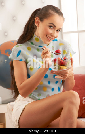 Schöne Brünette Modell genießen Sie gesunde frische Obstschale einschließlich Erdbeeren in hellen modernen home Szene. Stockfoto
