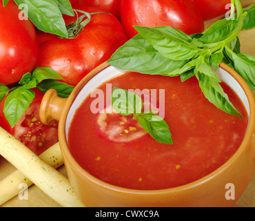 Tomatensuppe in Schüssel mit Tomaten und Basilikum in den Rücken (Tiefenschärfe) Stockfoto