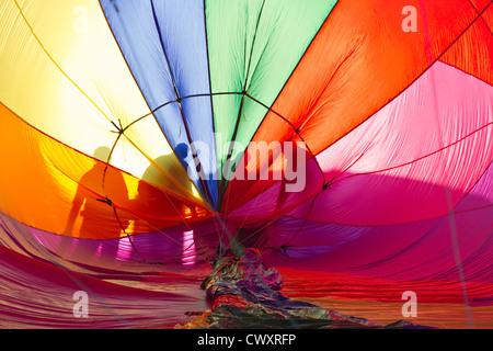 Ein Pilot und seine Crew ist den Ballon, die sie von der Morgensonne gegen den Stoff des Ballons silhouettiert sind Inspektion. Stockfoto
