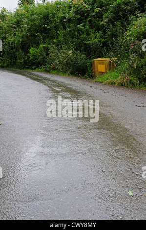 Regenwasser läuft Devon Gasse nach längeren Regenfällen.  Splitt-Box in Position für den Einsatz im Winter. Stockfoto