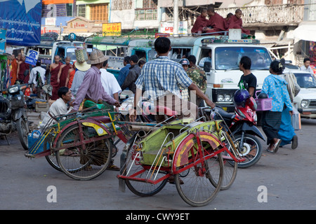 Myanmar, Burma, Mandalay. Neuling Mönche Reiten auf einem Lieferwagen in Mandalay Verkehr. Fahrradrikschas Passagiere warten. Stockfoto