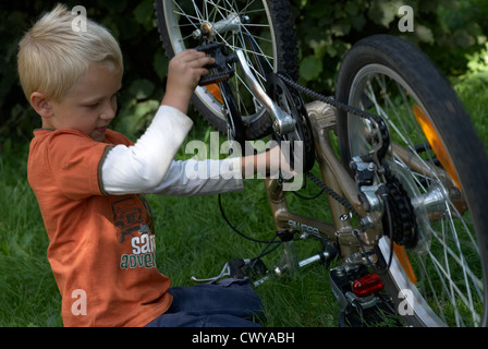 Kind blonde junge Prüfung und Festsetzung seines Fahrrades außerhalb Sommer Stockfoto