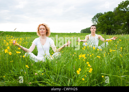 Junges Paar in der Wiese, Yoga zu praktizieren Stockfoto