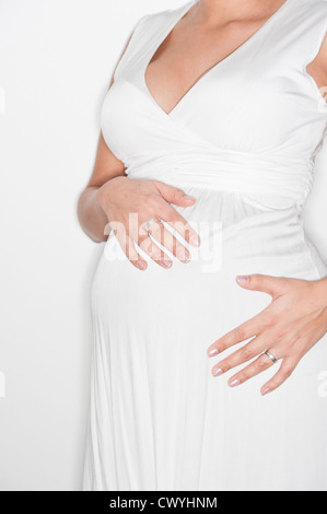 Schwangere Frau in einem weißen Kleid, halten ihre Hände auf den Bauch Stockfoto