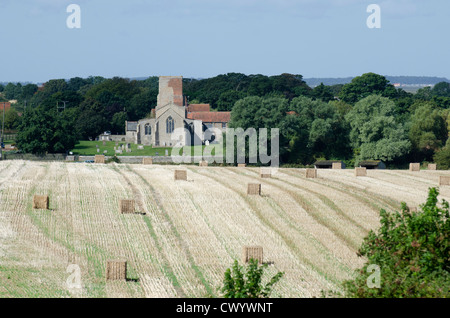 Abgeernteten Stoppelfeld mit Ballen, Morston All Saints Church in Hintergrund, Norfolk, England Stockfoto