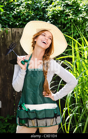 Glückliche junge Frau trägt Sonnenhut und Schürze im Garten Stockfoto