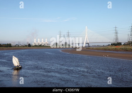 Ein Fischer Segel ein altes hölzernes Boot auf dem Fluss Dee mit Connah's Quay power station und Flintshire Bridge im Hintergrund. Stockfoto