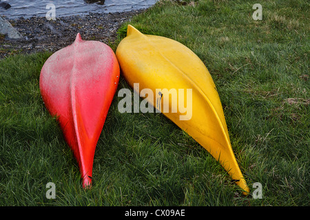 Eine rote und eine gelbe Kanu Seite an Seite ruht auf dem Gras neben einem See Stockfoto