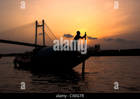 Ein Bootsmann segelt abends sein Boot über den Ganges in Kalkutta, Indien. Stockfoto