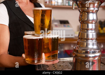 Geschickte Kellnerin hält vier frisch gefüllt Pint Gläser in der hand Stockfoto