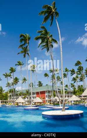 Pool mit Palmen gepflanzt in Wasser mit Stroh Schatten Hütten am Pool, Bavaro Punta Cana, Dominikanische Republik Stockfoto