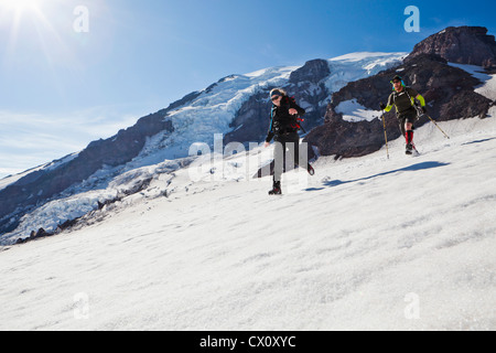 Ein junger Mann und eine Frau laufen und springen nach unten das Schneefeld Muir auf Mount Rainier, Washington, USA. Stockfoto