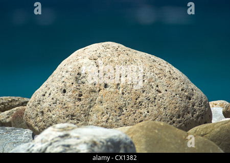 Nahaufnahme von einem großen Kieselstein auf einem Kiesstrand mit dem blauen Meer im Hintergrund Stockfoto