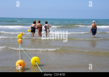 Rückansicht der drei Frauen in Führungspositionen und einen älteren Mann in brechenden Wellen im Meer, Punta Umbria, Costa De La Luz. Stockfoto