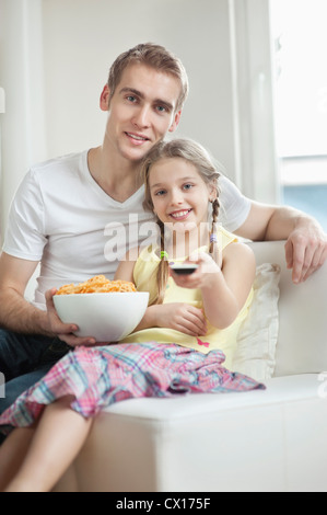 Porträt von Vater und Tochter vor dem Fernseher mit Schale voll Rad Form Snack-Pellets Stockfoto