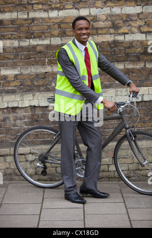 Glückliche junge männliche Ingenieur mit Fahrrad gegen Mauer Stockfoto