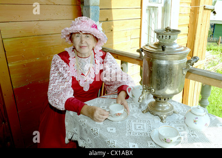 Die russische Frau in traditioneller Kleidung des 19. Jahrhunderts trinkt Tee aus dem Samowar. Aufgenommen am Juli 2012 in russischen Dorf meine Stockfoto