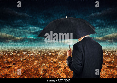 Geschäftsmann mit Regenschirm stehen in der Wüste während des Regens. Stockfoto