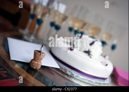 Sektkorken mit Münze eingefügt vor dem Hintergrund einer Hochzeitstorte und Champagner-Gläser Stockfoto