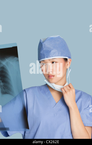 Weibliche Chirurg Blick auf Röntgen-Bericht über hellblauen Hintergrund Stockfoto