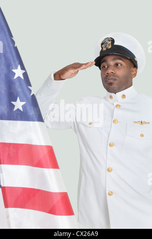 Porträt eines jungen US Navy-Offizier begrüßte amerikanische Flagge über dem grauen Hintergrund Stockfoto