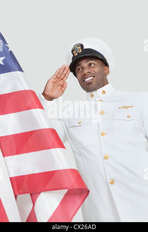 Porträt von glücklich junger US Navy Offizier begrüßte amerikanische Flagge über dem grauen Hintergrund Stockfoto