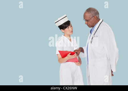Zwei Mediziner in Diskussion über ärztliches Gutachten vor hellblauem Hintergrund Stockfoto