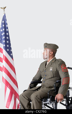 Jung uns Soldat im Rollstuhl Blick auf amerikanische Flagge über dem grauen Hintergrund Stockfoto