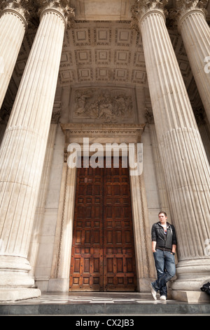 Man lehnt sich an eine der Säulen am Eingang zur St. Pauls Cathedral in London Stockfoto