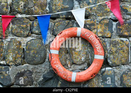 Rettungsring und Girlanden auf der alten Hafenmauer in Clovelly, Devon, England. (August) im Sommer 2012. Stockfoto