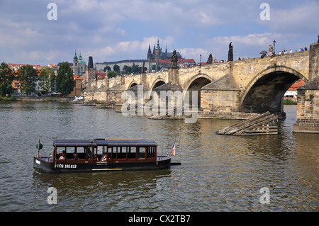 Ausflugsschiff auf der Moldau mit Karlsbrücke und Prager Burg im Hintergrund. Stockfoto