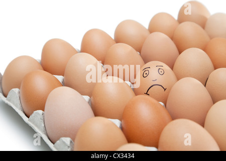 Trauriges Gesicht auf ein Ei umgeben von einfachen braunen Eiern im Karton vor weißem Hintergrund gezeichnet Stockfoto