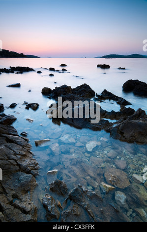 Blick auf das Meer bei Sonnenuntergang mit kristallklarem Wasser und Felsen und Steinen im Vordergrund Stockfoto