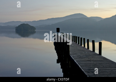 Horizontale Komposition, niedrige Lichtbild ein Steg auf einem ruhigen See mit einer kleinen Insel und Hügeln in der Ferne. Coniston. Stockfoto