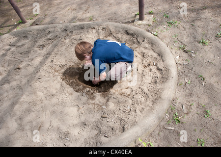 Acht Jahre alter Junge mit seinen Händen auf einem Spielplatz ein tiefes Loch zu graben. Stockfoto