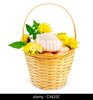 Eiern in einem Weidenkorb mit Blüten und Blättern des Löwenzahns ist isoliert auf weißem Hintergrund Stockfoto