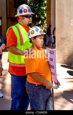 Seine bunten Sicherheitsausrüstung tragen, bringt ein Hispanic Vater seinen Sohn zu einer gewaltfreien Versammlung der lokalen Bauarbeiter. Stockfoto