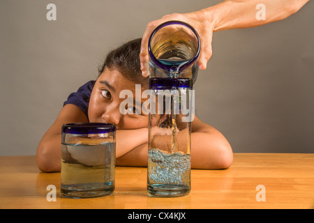 Ein Kind sieht bei identischen Gläser gefüllt mit der gleichen Menge Flüssigkeit Piagets flüssige Erhaltung Experiment nachweisen. Stockfoto