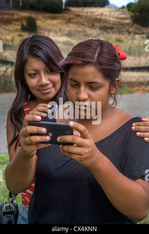 Eine aufgeregt hispanischen Mädchen liest eine Mobbing Nachricht auf ihr Smartphone, wie ihre Freundin sie tröstet. Stockfoto