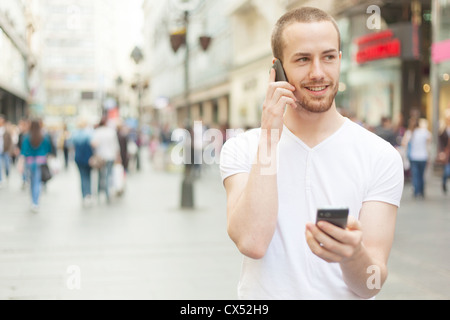 Männer in Händen zwei Handy, Stadtstraße und Menschen im Hintergrund halten Stockfoto