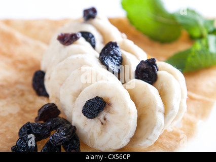 Gerollte dünne Pfannkuchen mit Banane und Rosinen Stockfoto