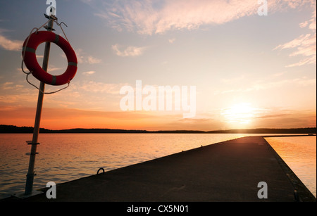 Sicherheitsausrüstung. Rettungsring auf dem Pier im orange sunrise Stockfoto