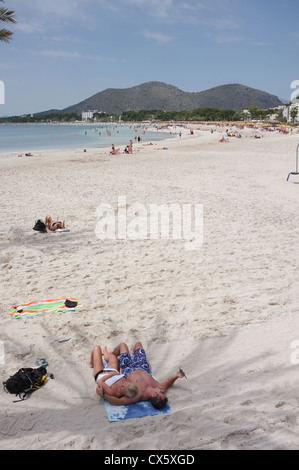 Ein paar liegen im Schatten einer Palme am kilometerlangen Strand von Port d Alcudia mallorca Stockfoto