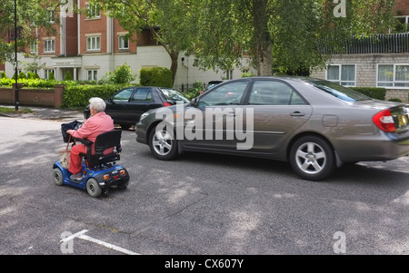Ein Rentner in einem behinderten Buggy Wagen fahren auf der Straße wird von einem Auto überholt. Stockfoto